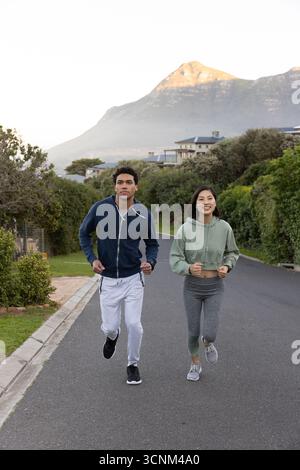 Verschiedene Paare, die gemeinsam auf der Straße in den Bergen in Hoodies und Laufschuhen joggen Stockfoto
