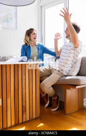Ein Paar sitzt auf einer eingebauten Bank am Fenster und überprüft Papierrollen auf einem Holztisch Stockfoto