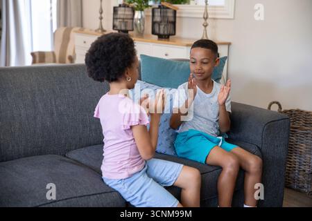 Verschiedene Geschwister spielen Handklatschspiel auf dem grauen Sofa im Wohnzimmer neben dem Konsolentisch Stockfoto