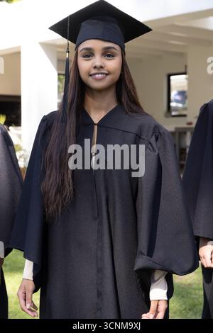 südasiatische Frau, die auf dem Rasen vor den Säulen des Campus steht, trägt ein schwarzes Kleid, Mörserplatte Stockfoto