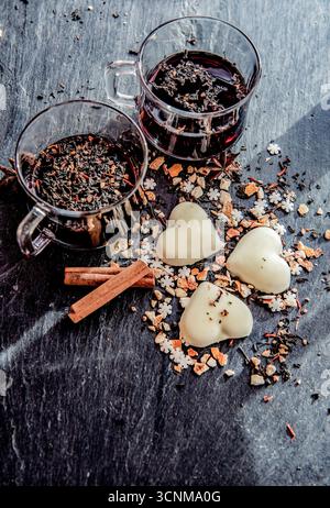 Glühwein in zwei Gläsern mit herzförmigen Keksen und Gewürzen auf grauem Schieferboden Stockfoto