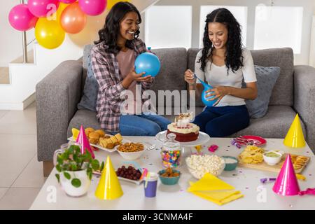Verschiedene Mutter und Teenager-Tochter sitzen auf Sofa im Wohnzimmer und teilen sich Kuchen Popcorn Stockfoto
