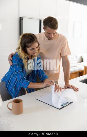 Paare, die auf der Kücheninsel die Zwischenablage durchblättern und Papiere mit Keramikbecher überprüfen Stockfoto