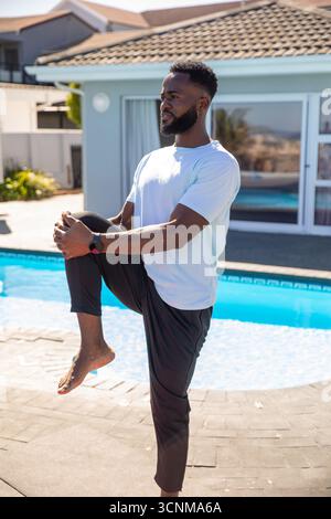 afroamerikaner, der sich von Knie bis Brust auf einer Steinterrasse neben dem Pool ausdehnt Stockfoto