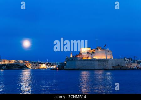 Das beleuchtete Fort St. Angelo steht am Grand Harbour in der Dämmerung von Malta, seine Kalksteinbastionen leuchten unter einem blauen Abendhimmel und Vollmond. Stockfoto