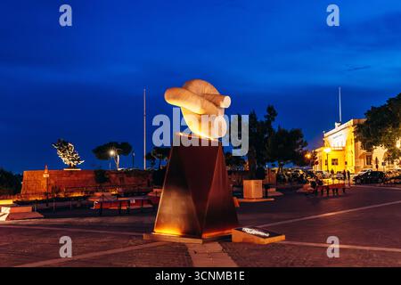 Valletta, Malta – 13. April 2025: Beleuchtete zeitgenössische abstrakte Skulptur auf einem öffentlichen Platz in der Abenddämmerung, mit dramatischem blauem Himmel und markantem A Stockfoto