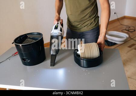 Abgeschnittener Schuss des männlichen Reinigungstisches mit Luftbefeuchter unter Verwendung eines Handsaugers, wobei der Staub vorsichtig aus dem Filter und den internen Komponenten für entfernt wird Stockfoto