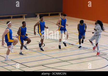Verschiedene männliche Basketballteams in Uniformen, die hohe Knie mit Linien auf dem Spielfeld trainieren Stockfoto