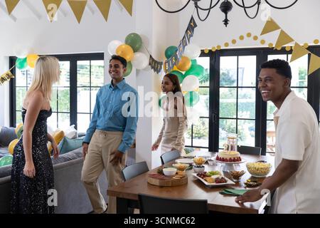 Verschiedene Freunde feiern Geburtstag im Speisesaal zu Hause um den Tisch mit Kuchen, Ballons Stockfoto