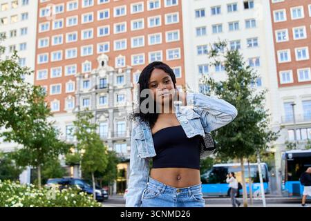 Stilvolle junge Frau posiert selbstbewusst mit der Hand am Hals vor dem Hintergrund eines Luxushotels in madrids pulsierendem Stadtzentrum Stockfoto