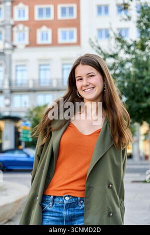 Stilvolle junge Frau lächelt in einem modischen, legeren Outfit selbstbewusst in einem urbanen Ambiente Stockfoto
