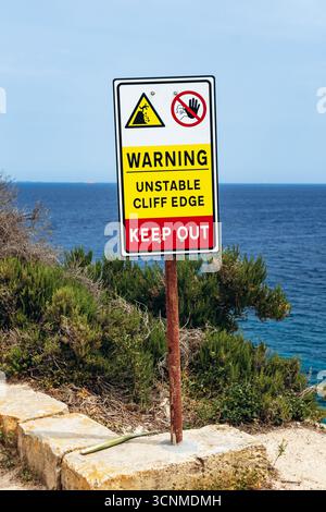 Küstenpfad zwischen Marsaskala und Marsaxlokk, Malta. Warnschild, das auf instabile Klippenkante und Gefahr mit Blick auf das Mittelmeer hinweist Stockfoto