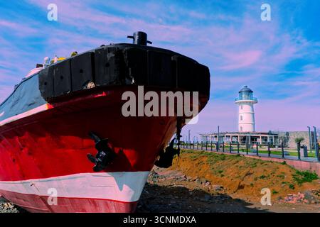 Rotes und schwarzes Schiff dockte in der Nähe des White Lighthouse an. Ein markantes rot-schwarzes Schiff legt an einem sonnigen Tag in der Nähe eines weißen Leuchtturms an. Stockfoto