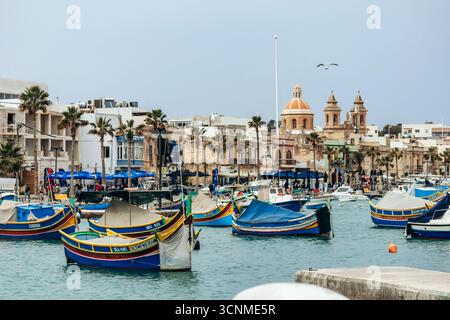 Marsaxlokk, Malta - 13. April 2025: Traditionelle, farbenfrohe maltesische Fischerboote, genannt Luzzu, mit leuchtend blauen, gelben und roten Details, die in der verankert sind Stockfoto