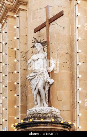 Aus nächster Nähe sehen Sie eine weiße Statue von Jesus Christus mit einem Holzkreuz, die an der Ecke einer historischen Kirchenfassade in Valletta ausgestellt ist Stockfoto