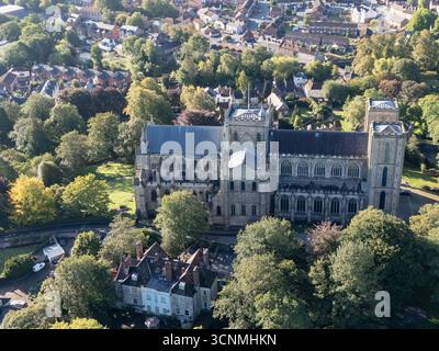 Luftaufnahme der Kathedrale von Ripon in Ripon, North Yorkshire, Großbritannien, aufgenommen bei klarem Spätsommerwetter mit hellblauem Himmel und warmem Sonnenlicht, das die beeindruckende gotische Architektur der Kathedrale unterstreicht. Das Bild zeigt die elegante frühe englische Westfront mit ihren Doppeltürmen, komplizierten Mauerwerken und bogenförmigen Fenstern, umgeben von den historischen Straßen der Stadt, nahe gelegenen Gebäuden, Dächern und Grünflächen einschließlich Parks und offenen Bereichen. Dieser Blick über der Drohne fängt die zentrale Position der Kathedrale in der kompakten mittelalterlichen Stadt ein und betont ihre Rolle als wichtiges Wahrzeichen des Kulturerbes Stockfoto