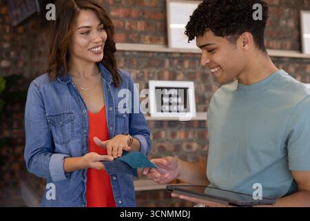 Verschiedene Kollegen vergleichen blaue Farbfelder und Farboptionen auf dem Tablet neben dem Leuchtkasten-Schild Stockfoto