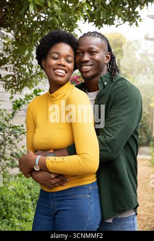 Zusammen im Garten stehend, afroamerikaner-Paar umarmt, lächelt und Armbanduhr sichtbar Stockfoto