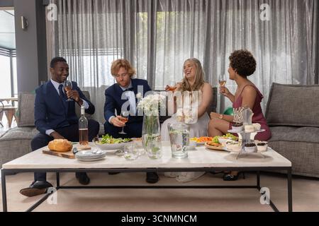 Verschiedene Hochzeitsfeiern in formeller Kleidung, die Vorspeisen essen und Weingläser auf dem Sofa in der Lounge halten Stockfoto