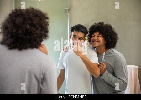Verschiedene männliche Freunde putzen sich die Zähne im modernen Waschbecken im Badezimmer mit Zahnbürsten und Handtuchhalter Stockfoto