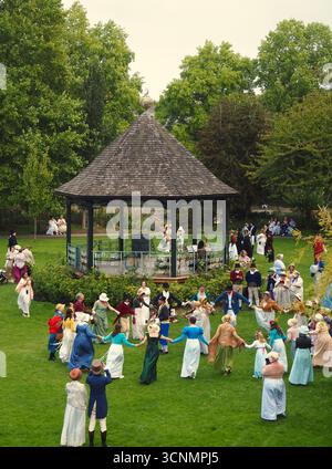 Die in Regentalkostümen gekleideten Menschen bereiten sich auf einen traditionellen Tanz im Parade Gardens Bath bei der Jane Austen Festival Parade 2025 vor. Stockfoto