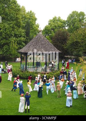 Die in Regentalkostümen gekleideten Menschen bereiten sich auf einen traditionellen Tanz im Parade Gardens Bath bei der Jane Austen Festival Parade 2025 vor. Stockfoto