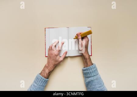 Top-down-Ansicht eines Mannes, der Notizen in einem Bullet Journal macht. Kreatives Schreiben, Planen und Leere-Page-Syndrom auf einem isolierten Modell. POV isoliert. Stockfoto