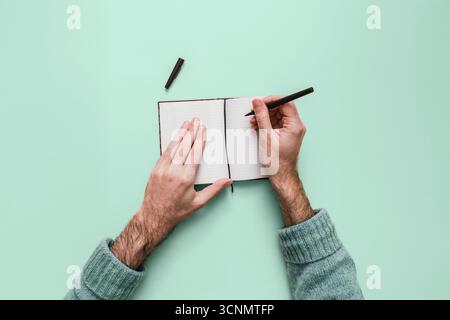 Top-down-Ansicht eines Mannes, der Notizen in einem Bullet Journal macht. Kreatives Schreiben, Planen und Leere-Page-Syndrom auf einem isolierten Modell. POV isoliert. Stockfoto
