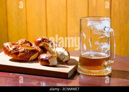 Bier und Brezel auf dem Tisch. oktoberfest feiern. Glasbecher mit kaltem Getränk und gebackenen Salzsnacks auf hölzernem Hintergrund. Rustikale Szene Stockfoto