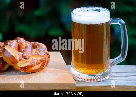 Bier und Brezel im Freien trinken. Feiern Sie das oktoberfest. Glasbecher mit kaltem Getränk auf dem dunklen Hintergrund des Gartens. Rustikale Szene Stockfoto