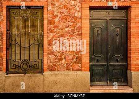 Dunkelgrüne Metalltür und Fensterläden an der verwitterten Steinfassade des historischen Puertollano House Stockfoto