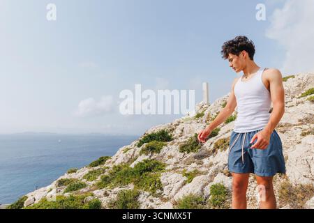 Ein Teenager steht auf der Spitze des Berggipfels und blickt im Sommer über das Meer Stockfoto