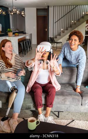 Verschiedene weibliche Freunde spielen Virtual-Reality-Spiel auf Sofa im Wohnzimmer mit Controllern Stockfoto