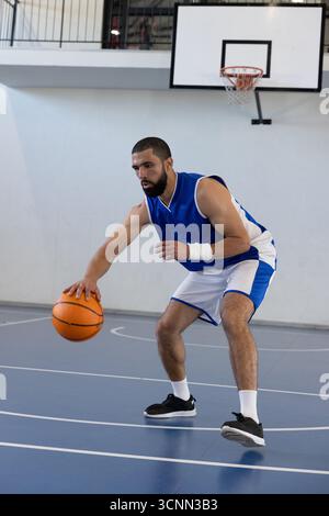 Erwachsener männlicher Basketballspieler dribbelt orangen Ball in Ausrüstung auf dem Platz unter dem Korb, Geländer Stockfoto