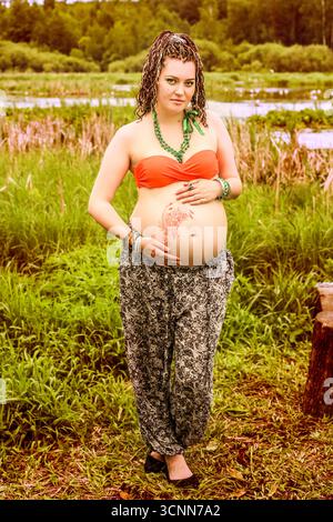 moskau, russland, 29.05.2015 schwangere Frau mit traditionellem Henna auf dem Bauch steht auf einem Feld. Werdende Mutter in ethnisch inspiriertem Outfit. Stockfoto