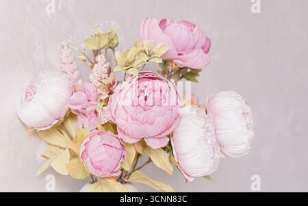 Künstliches Pfingstrosen-Bouquet mit pastellrosa und weißen Blumen in zarter Anordnung auf hellem Wandhintergrund. Trendiges Blumendekor, Frühlingsinspirierung, Stockfoto