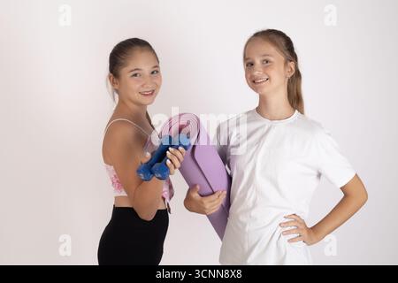 Mädchen in weißen Hemden und schwarzen Hosen, die lila Yogamatten halten Stockfoto