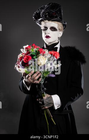Ein junger Mann zeigt sein ausgeklügeltes Halloween-Kostüm mit einem bunten Blumenstrauß. Stockfoto