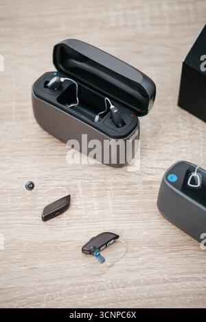 Moderne digitale Hörgeräte mit Ladetasche auf Holztisch in der audiologischen Klinik. Hörgerät, Ladegerät und Ohrmodell zur Anbringung und Demonstration. Stockfoto