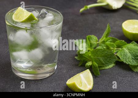 Beschlagenes Glas mit Kalk und Eis. Minzzweige und Limettenhälften auf dem Tisch. Schwarzer Hintergrund. Draufsicht Stockfoto