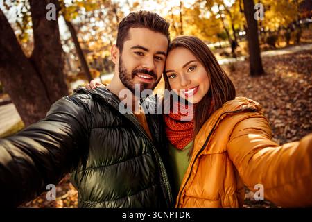 Ein lächelndes Paar genießt einen Herbsttag im Park, umgeben von lebhaftem Laub und warmem Sonnenlicht bei einem romantischen Spaziergang Stockfoto