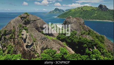 Üppige Vegetation bedeckt steile vulkanische Hänge mit Blick auf eine wunderschöne tropische Lagune auf Kuata Island, Yasawa Inselgruppe, Fidschi, an einem sonnigen Sommertag. Drohnenflug Stockfoto