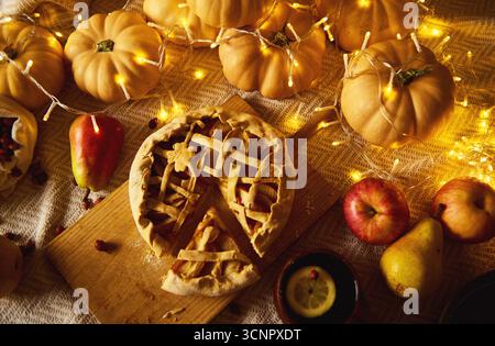 Eine warme herbstliche Thanksgiving-Szene mit einem Gitterkuchen auf einem Holzbrett, Kürbissen, Äpfeln und Feenlichtern, die eine gemütliche Erntestimmung schaffen. Stockfoto