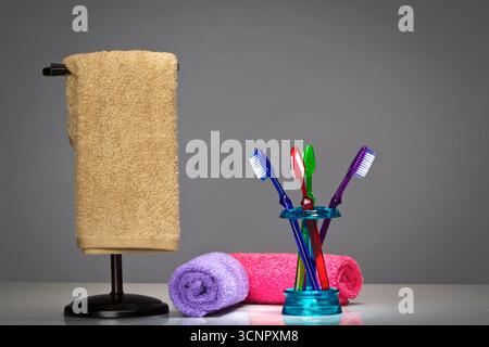 Farbenfrohe Zahnbürsten sind mit einem Stapel leuchtender Handtücher in einem Studio angeordnet, die vor einem sauberen Hintergrund erfasst werden und helle Farben und weiche Farben hervorheben Stockfoto