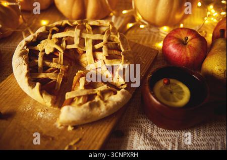 Eine warme Herbstszene mit einem Gitterkuchen auf einem Holzbrett, Äpfeln, Birnen und Zitronen in einem Becher, leuchtenden Lichtern und einer gemütlichen Thanksgiving-Stimmung. Stockfoto