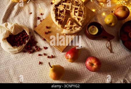 Gemütlicher Herbsttisch mit einem Gitterkuchen auf einem Holzbrett, Preiselbeeren aus einem Stoffbeutel, Äpfeln und Birnen und einem warmen Getränk mit le Stockfoto
