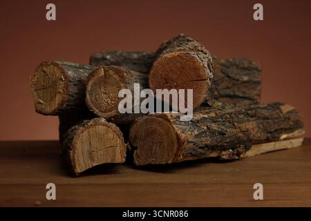 Haufen von geschnittenem Brennholz auf Holztisch vor braunem Hintergrund, Nahaufnahme Stockfoto