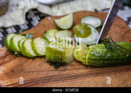 Ein Nahbild einer Person, die frische Gurken auf einem rustikalen hölzernen Schneidebrett schneidet Stockfoto