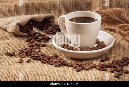 Eine warme und einladende Kaffeeszene mit einer wunderschön gefertigten Tasse Kaffee, umgeben von kräftigen Kaffeebohnen, alles gegen eine strukturierte Rückseite Stockfoto