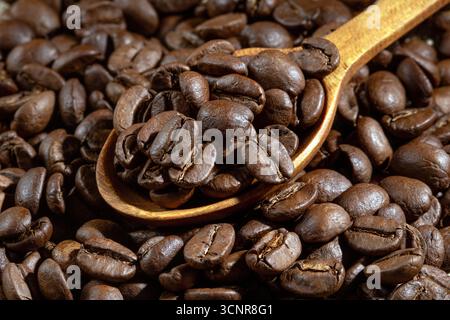 Dieses Bild zeigt eine Nahaufnahme eines wunderschön gearbeiteten Holzlöffels, gefüllt mit aromatischen Kaffeebohnen, die die reichhaltigen Texturen und Farben betonen Stockfoto